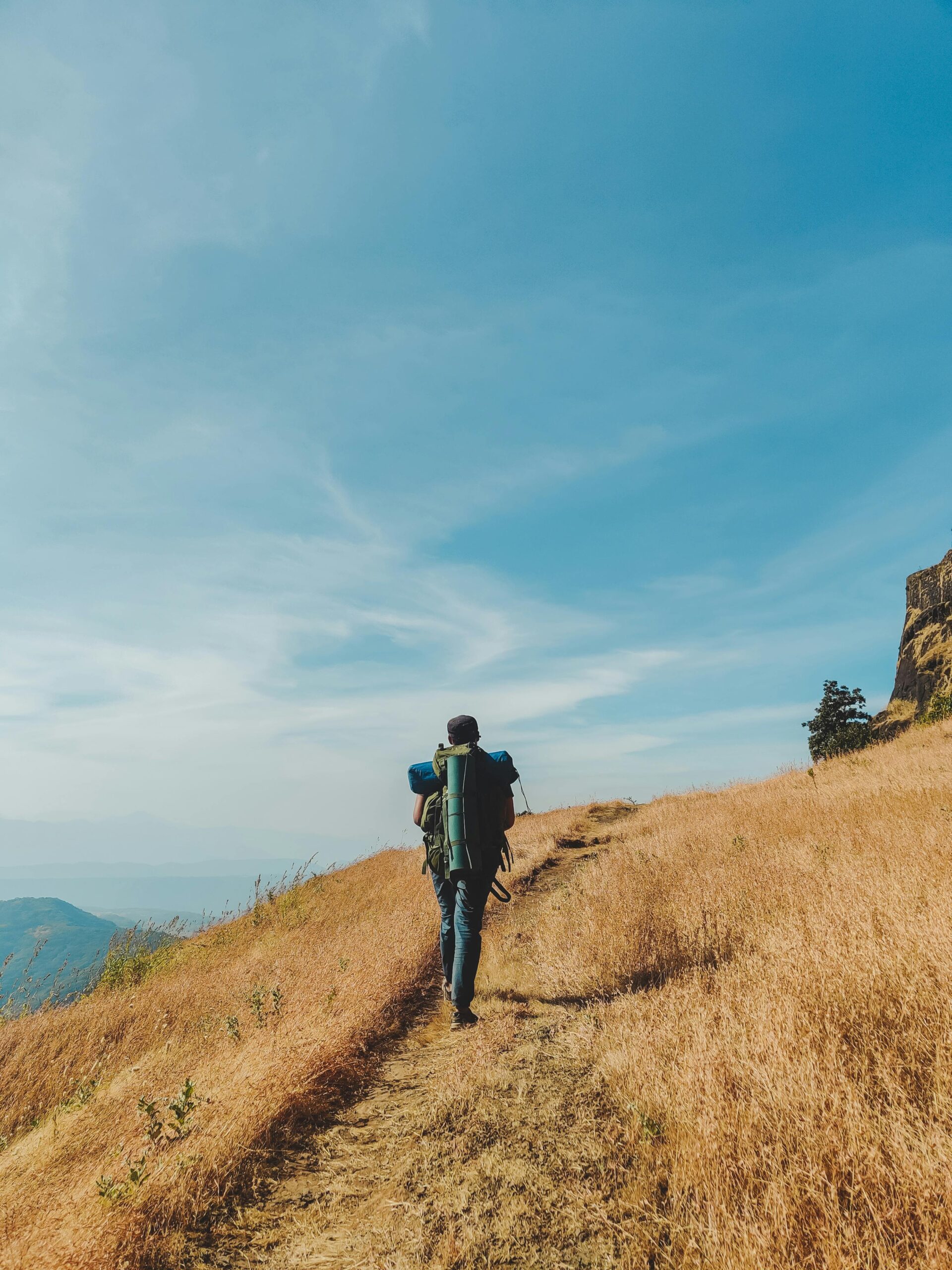 A lone traveler hikes through a scenic mountain trail under a clear sky.